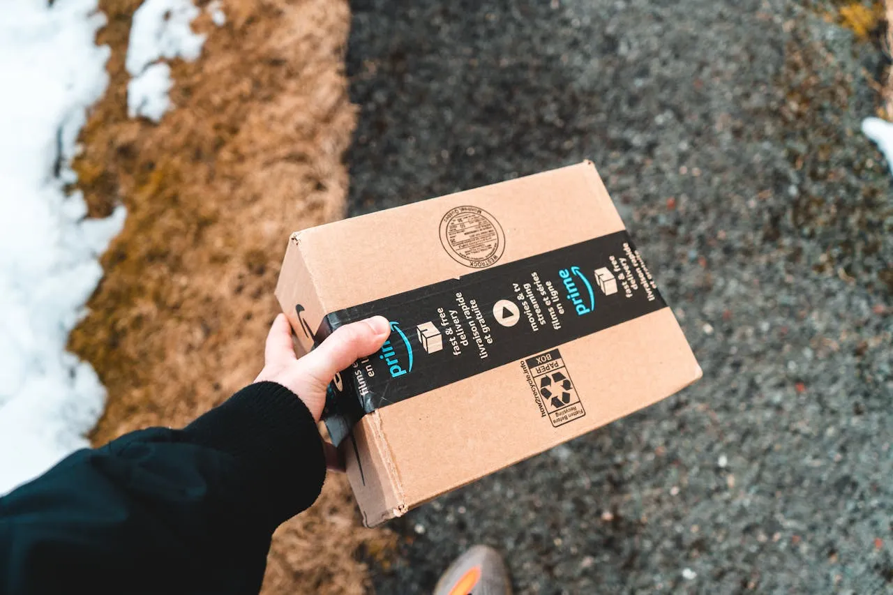 A delivery man carries an Amazon package on a snowy street.
