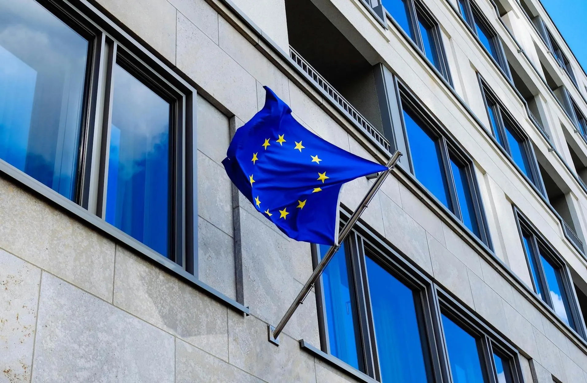 An office building reflecting the blue sky holds an EU (European Union) flag.