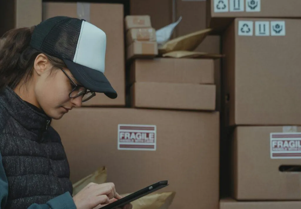 A delivery driver uses a tablet in front of a van full of packages in cardboard boxes.
