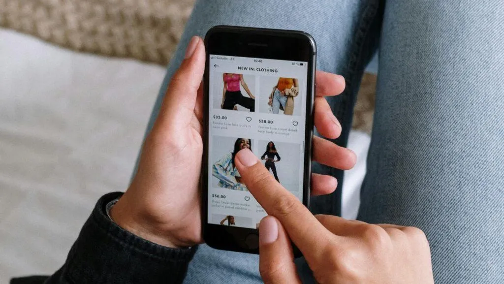 person wearing jeans scrolls through clothing items on a mobile phone.